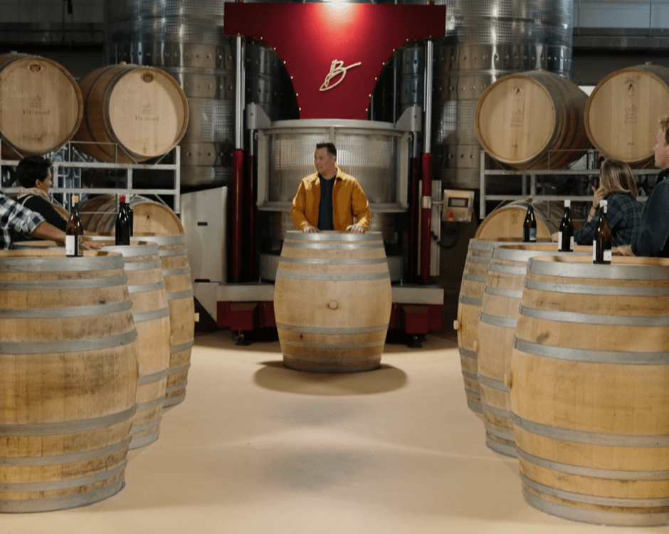 Episode 6 - Die Top 3 Word Aangekondig! illustrated by the contestants and host standing around wine barrels during the recording