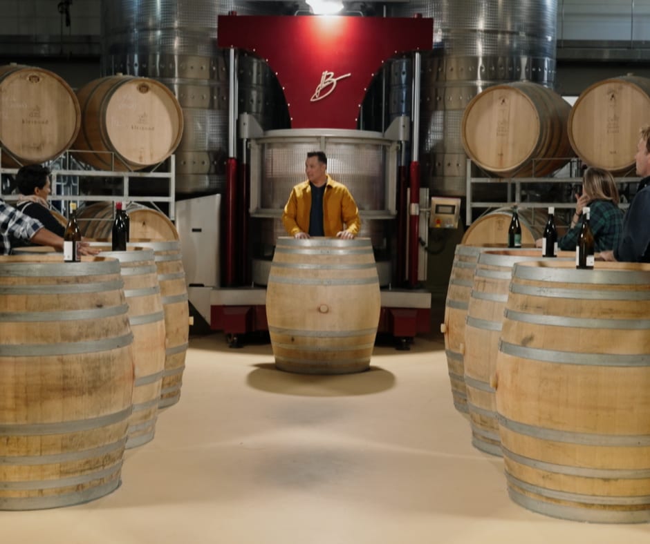 Episode 6 - Die Top 3 Word Aangekondig! illustrated by the contestants and host standing around wine barrels during the recording